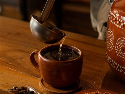 Café de olla servido desde una jarra de barro, con canela y piloncillo