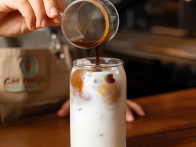 Café latte con hielo en vaso alto, con espresso vertiéndose sobre la leche