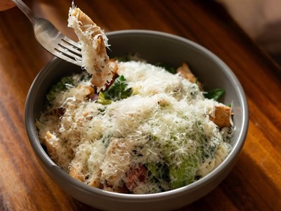 Ensalada de pollo y pasta con hojas verdes, crutones y queso parmesano