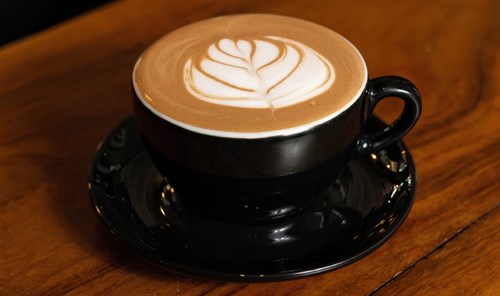 Latte con arte de leche en taza negra sobre la barra de Cafferium